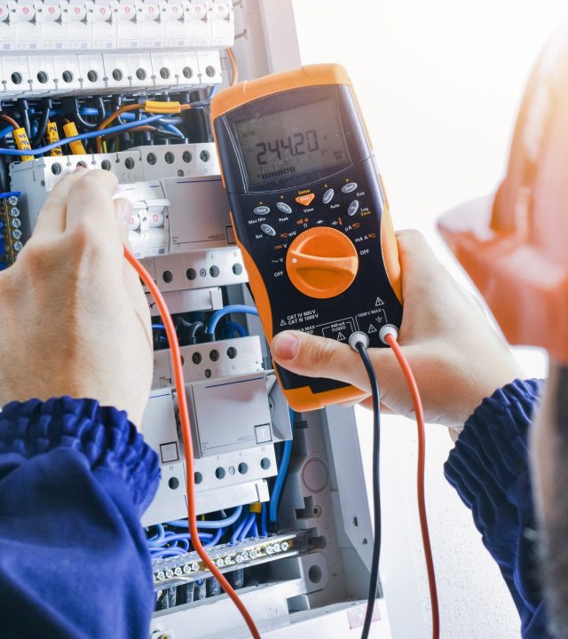 Electrician installing electric cable wires of fuse switch box. Multimeter in hands of electricians detail.